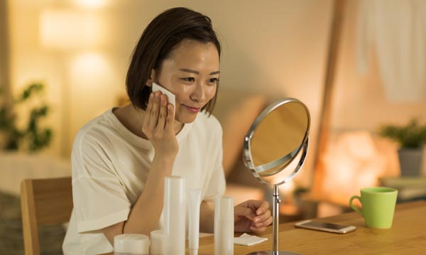 夜、スキンケアを鏡の前でする女性