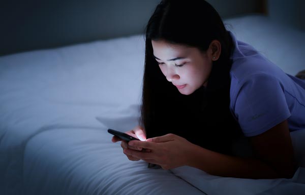 夜ベッドでスマホをみる女性