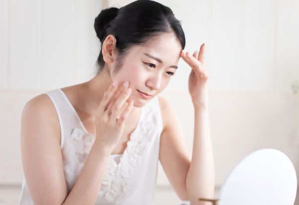鏡で顔の肌をチェックし悩む女性
