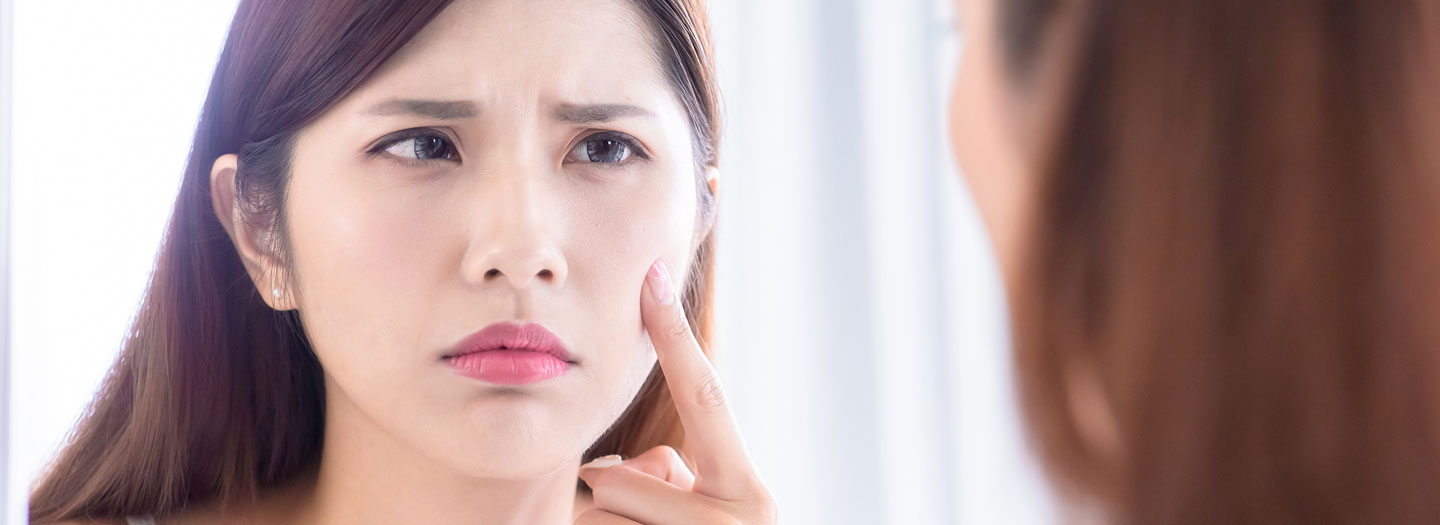 鏡で自分の頬の肌状態を困り顔で見る女性