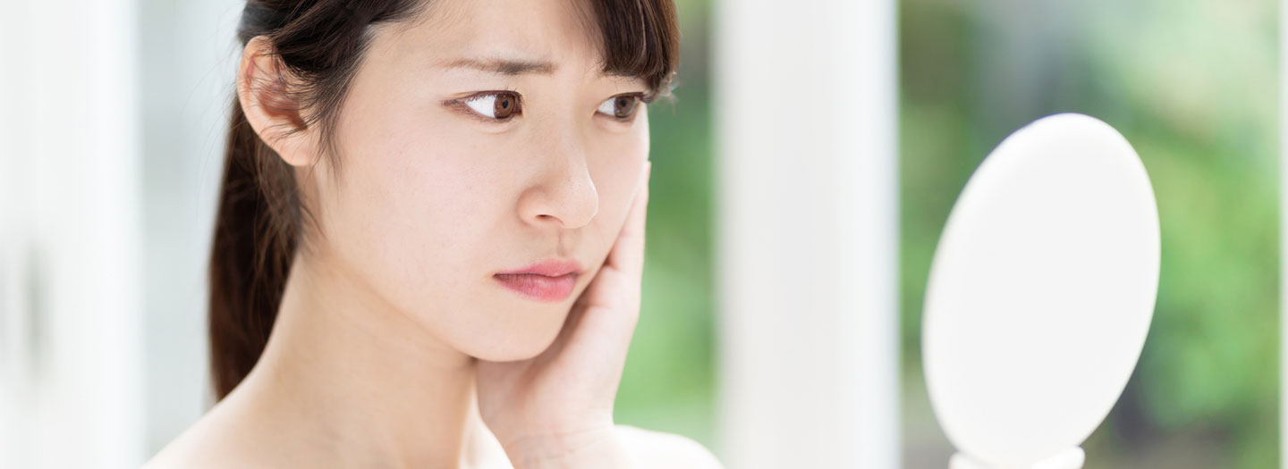 鏡で自分の肌状態を困り顔で見る女性