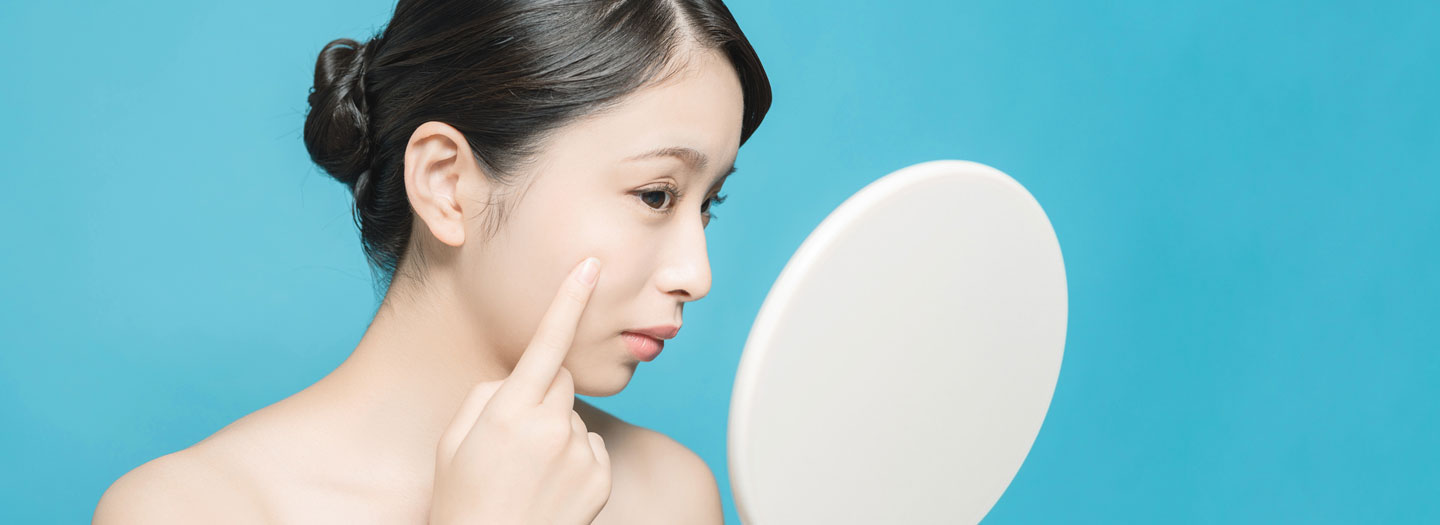 鏡で自分の肌をチェックする女性