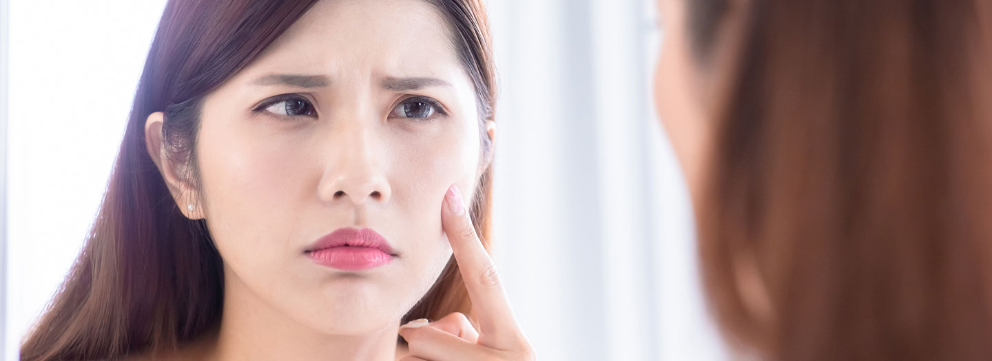 困り顔で鏡で自分の肌をチェックする女性