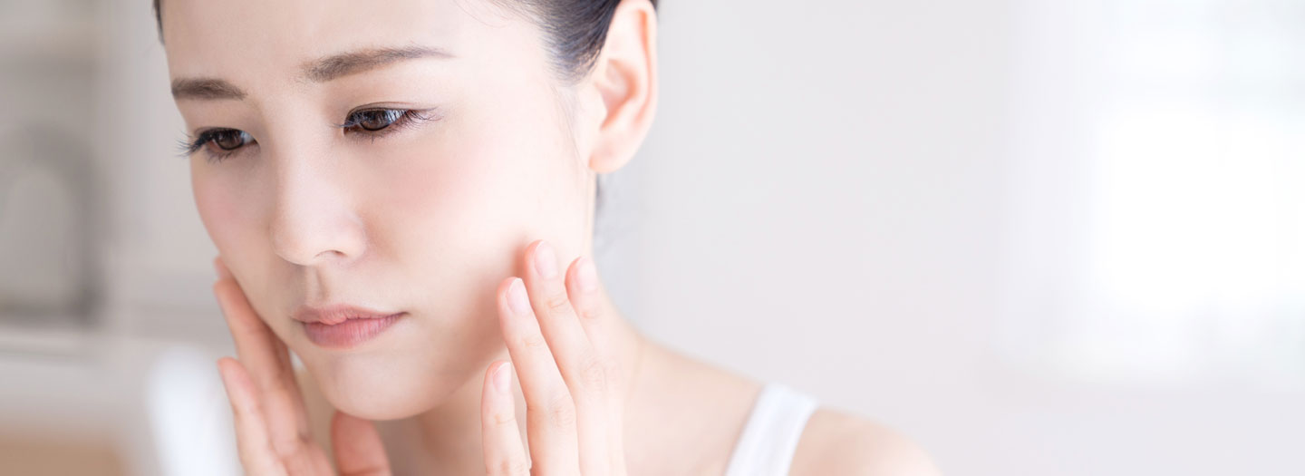 困った顔で顔の肌をチェックする女性