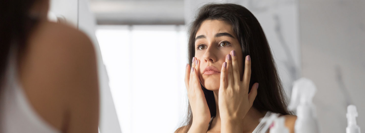 浴室の鏡で自分の肌を見て悲しい顔で肌に触れる若い女性