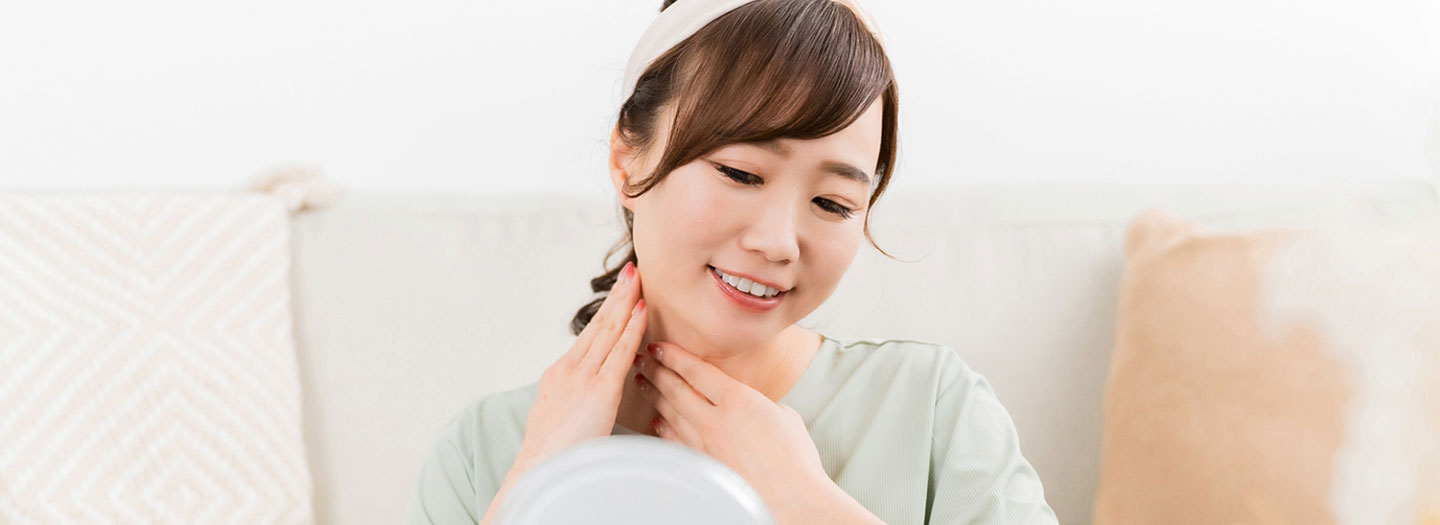 鏡を見ながら首のスキンケアをする女性