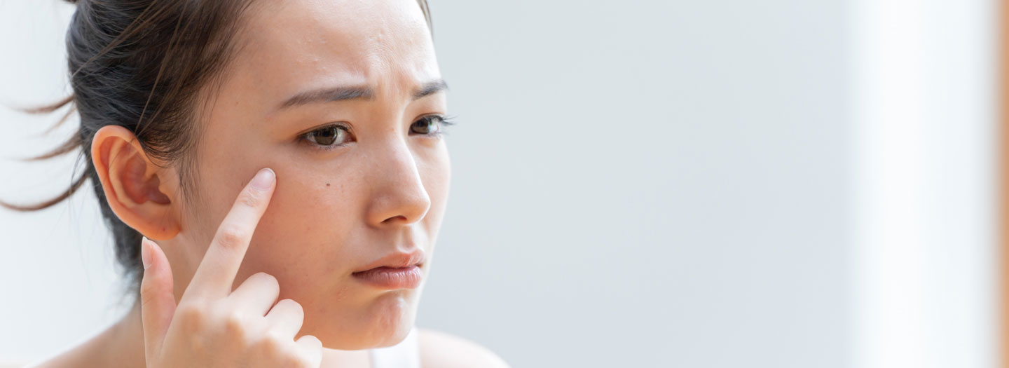 鏡で自分の目の下のくすみを気にする女性