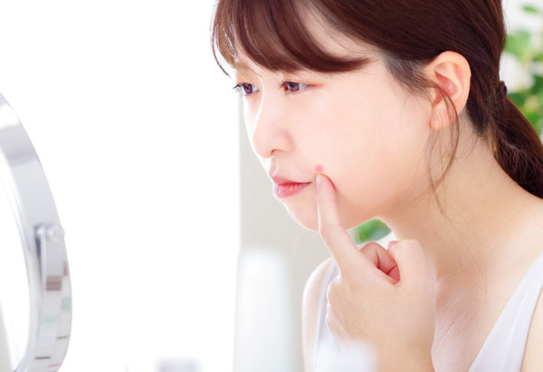 鏡でニキビを見る女性